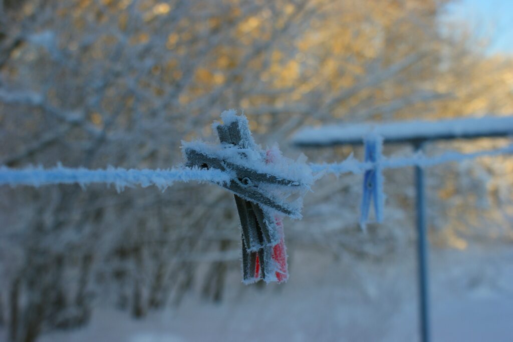 Tøjklemme dækket af rimfrost hænger på en snor i vinterlandskab med slørede træer i baggrunden.