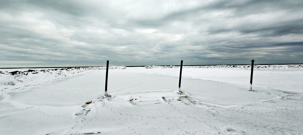 Frossen havneindsejling ved Hou i Nordjylland med tre pæle, sne og grå vinterhimmel.